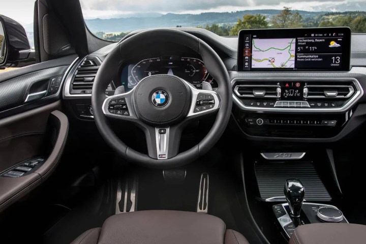 BMW car interior with steering wheel, digital dashboard, and infotainment screen showing a map.